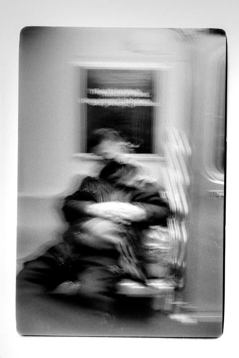 A blurry figure of a person is seated on a moving train, with a window visible in the background.
