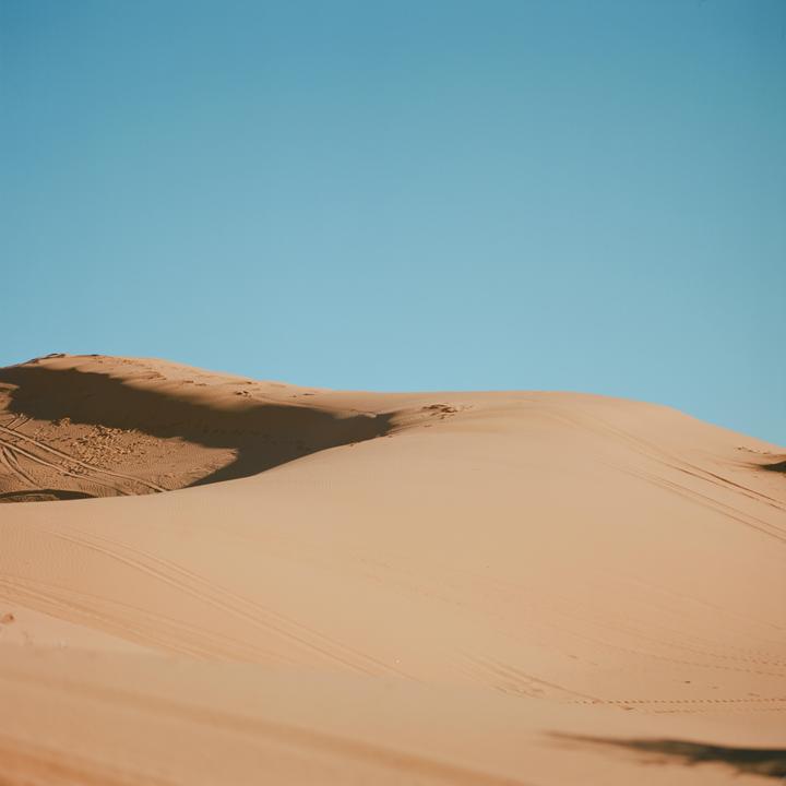 A large sand dune casts a shadow under a clear blue sky.