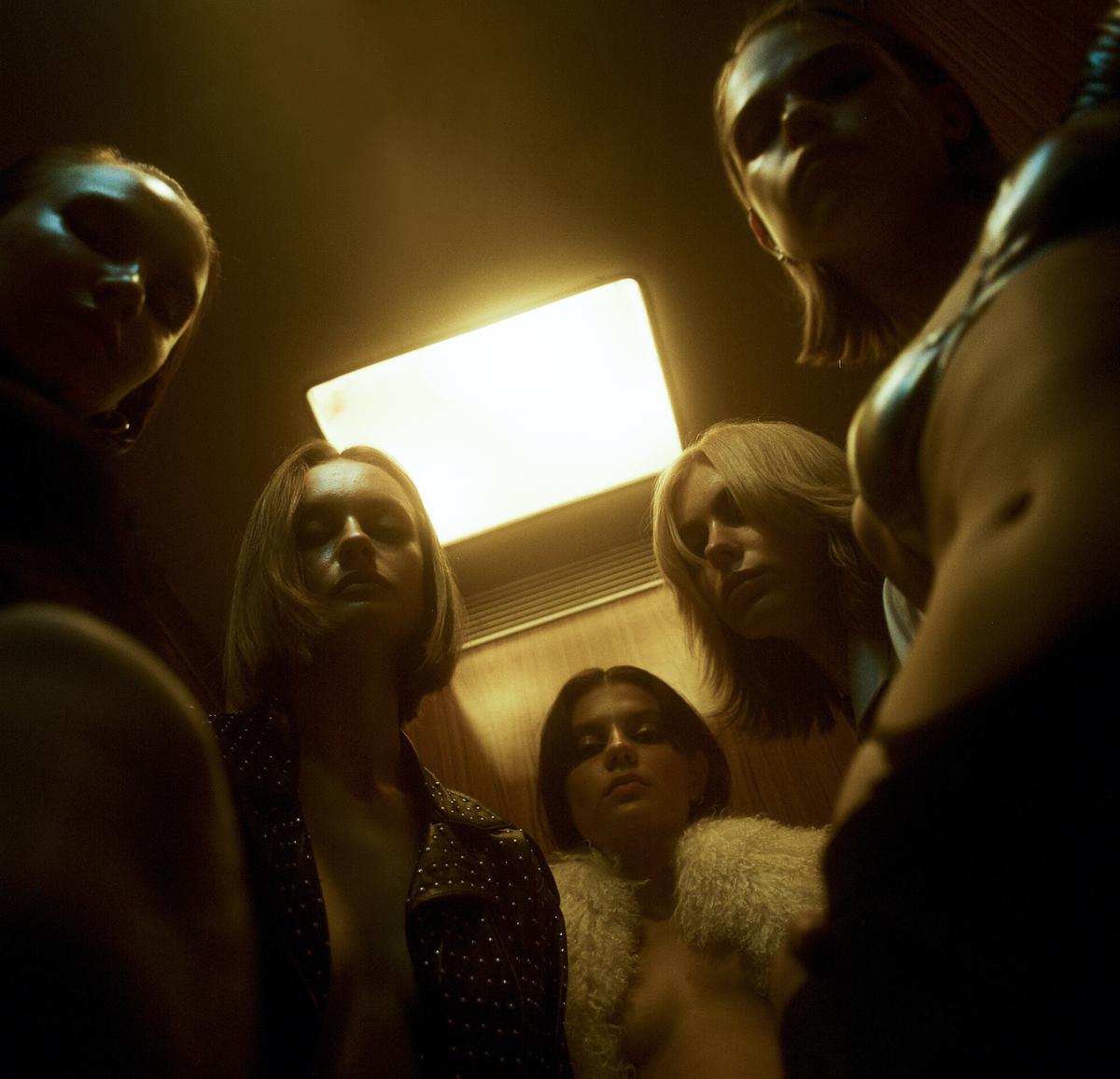 Five women are looking down at the camera in an elevator.