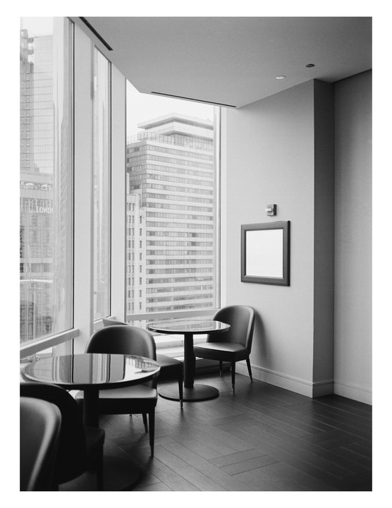A hotel lounge area with small tables and chairs is visible next to a large window overlooking city buildings.