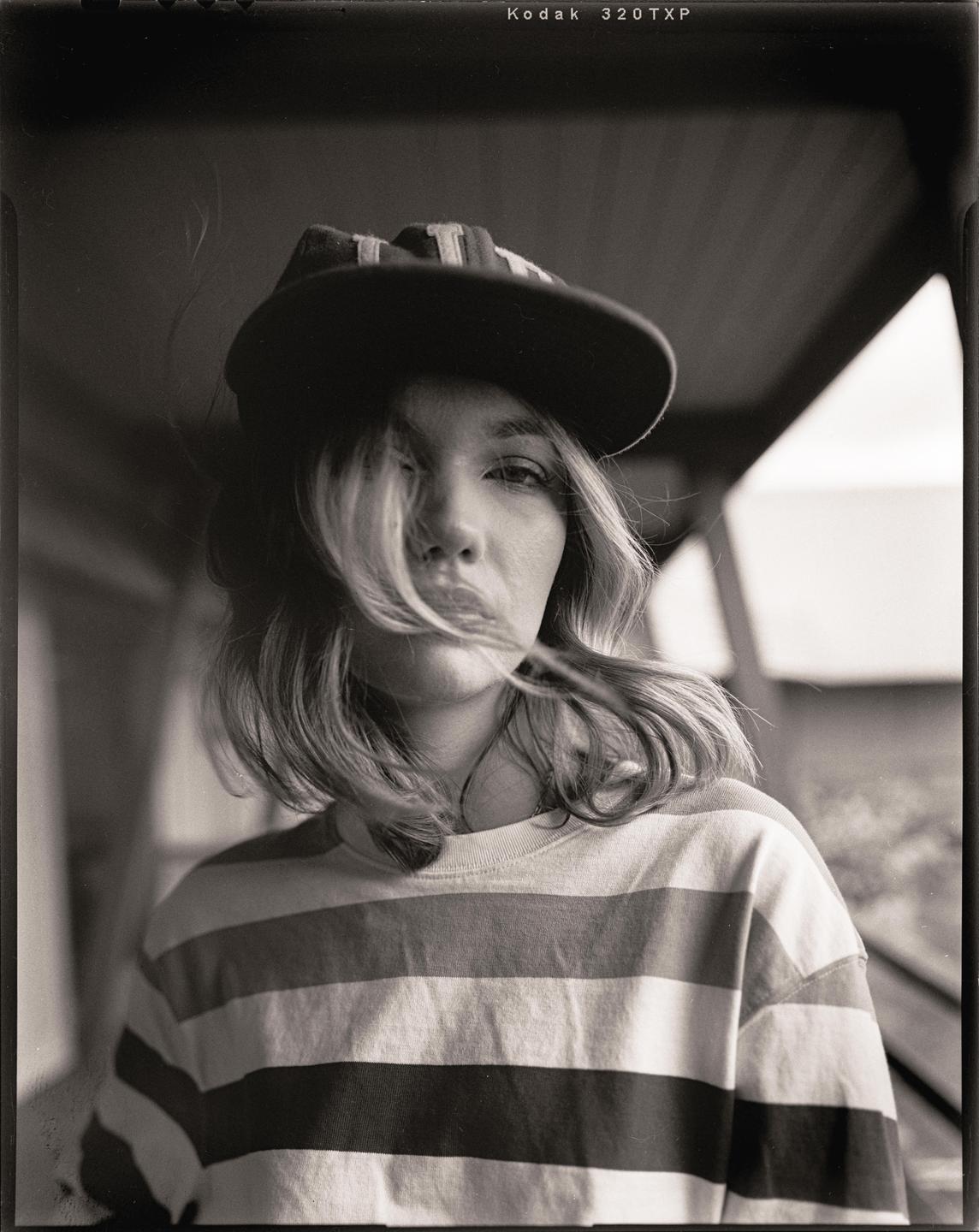 A woman wearing a striped shirt and a baseball cap looks directly at the viewer.