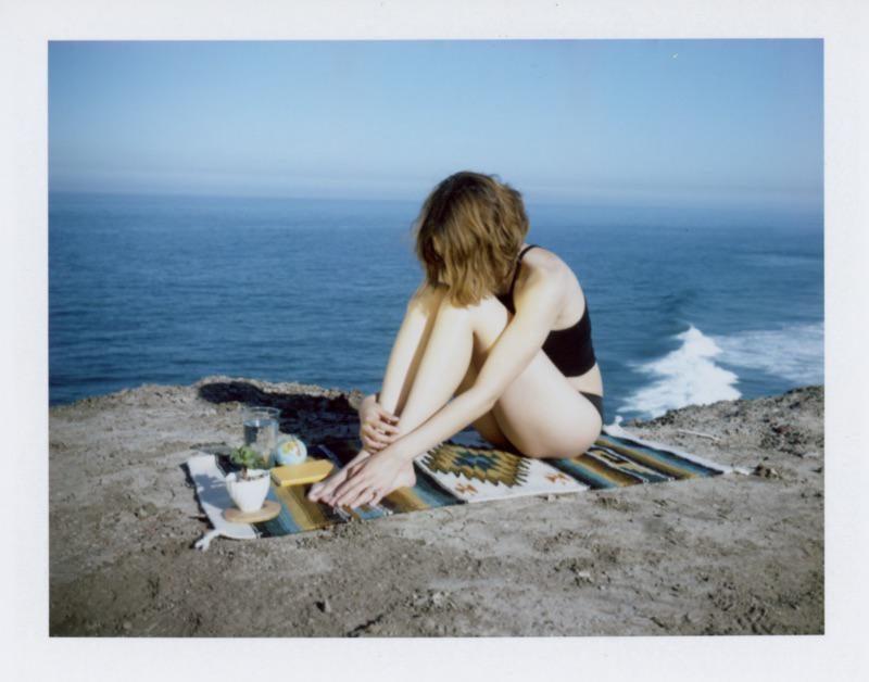 A woman sits on a blanket on a cliff overlooking the ocean.
