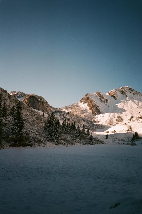 A snow-covered mountain landscape with evergreen trees and small buildings in the distance is visible under a clear sky.