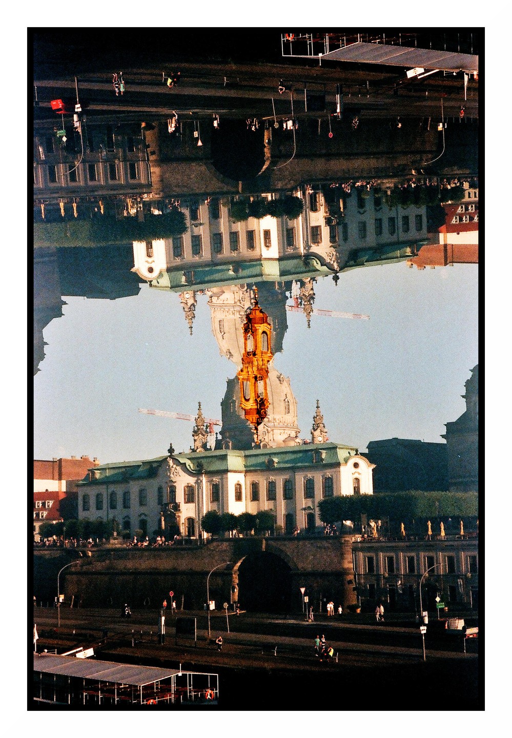 A double exposure shows a building with a dome and a golden tower reflected upside down over itself, with people and a boat visible at the bottom.