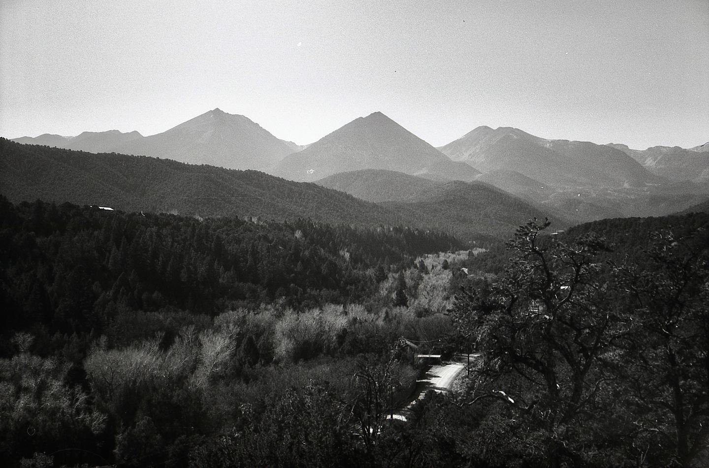 A winding road leads through a valley of trees towards distant mountains under a hazy sky.