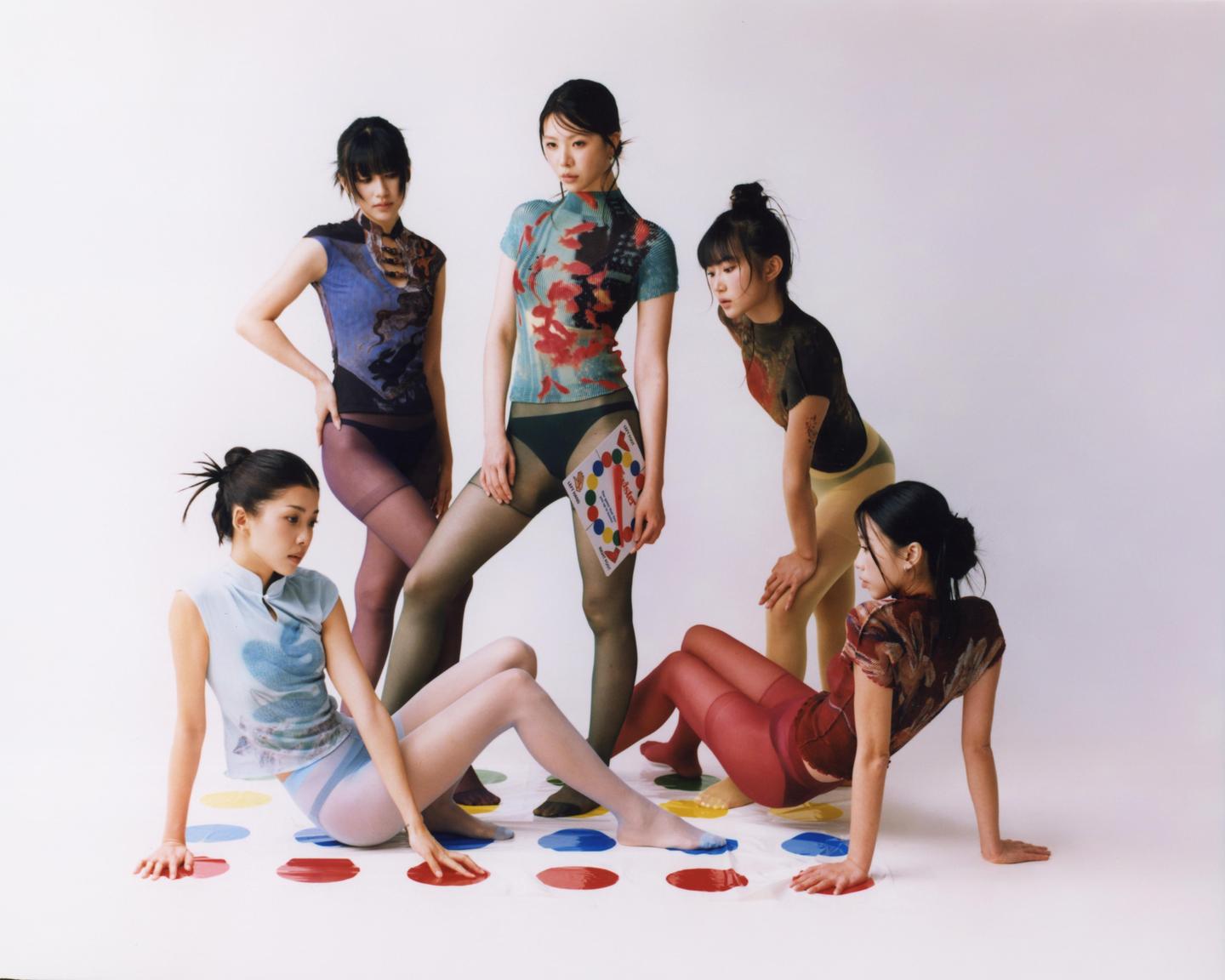 Five women are playing Twister on a white floor.