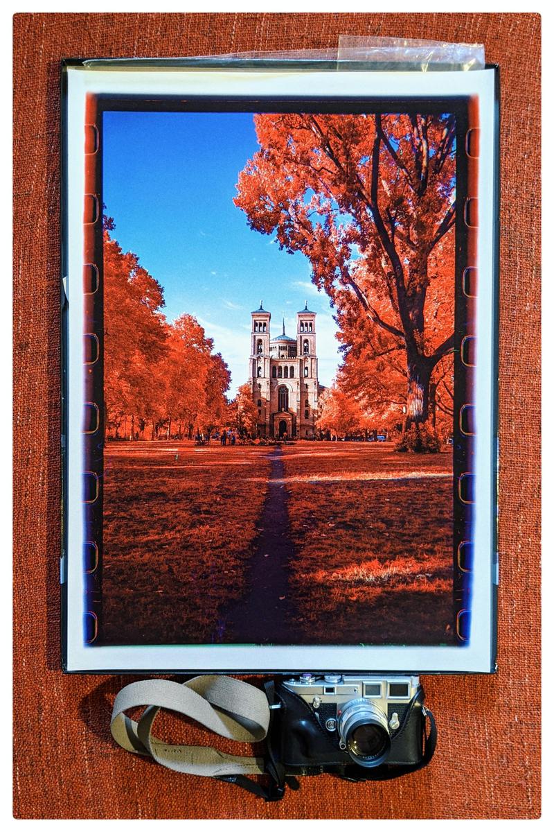 A print of a building with two towers and red trees is displayed with a camera.