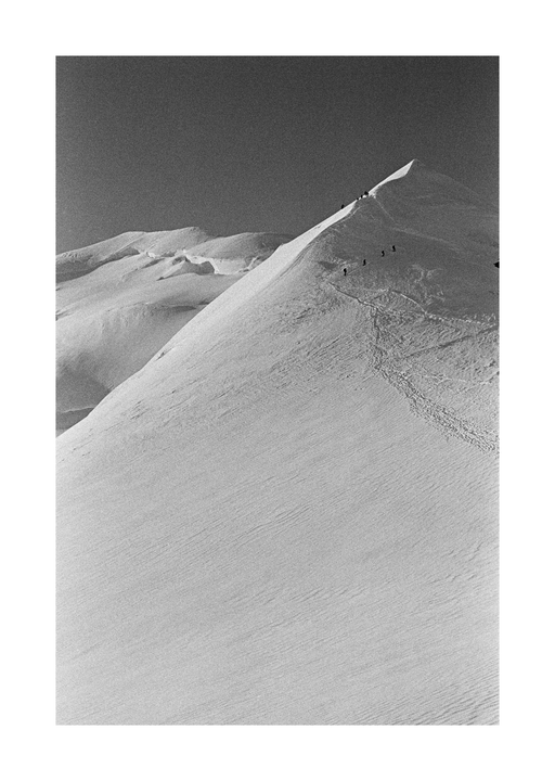 A group of people ascend a snow-covered mountain peak under a clear sky.