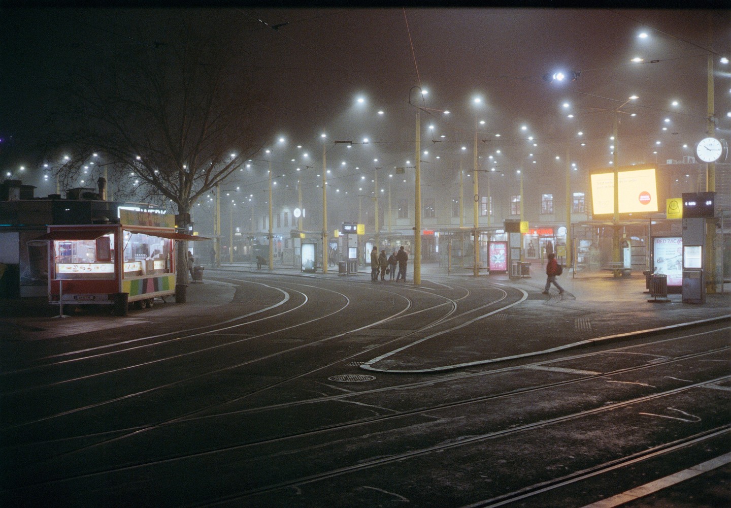 A street food stall and tram tracks are visible on a foggy night in Graz.