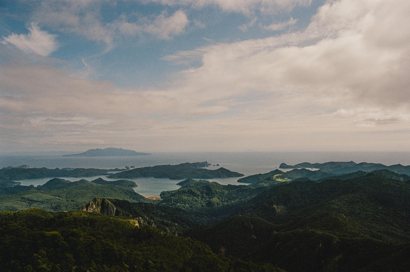 A vast landscape shows a series of green, forested islands and peninsulas extending into a calm body of water under a cloudy sky.