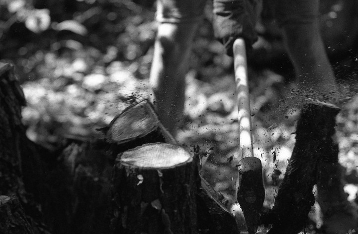 An axe splits a log, sending wood chips flying.