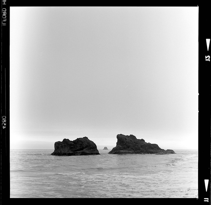 Two large rock formations emerge from the ocean under a bright, overcast sky.