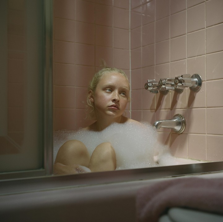 A girl sits in a bubble bath in a pink tiled bathroom.