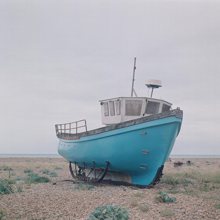 A blue boat sits on a rocky beach under a cloudy sky.