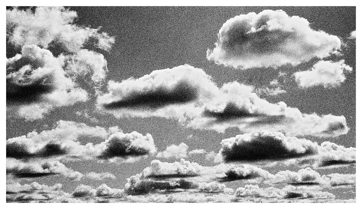 A black and white image shows a sky filled with cumulus clouds.