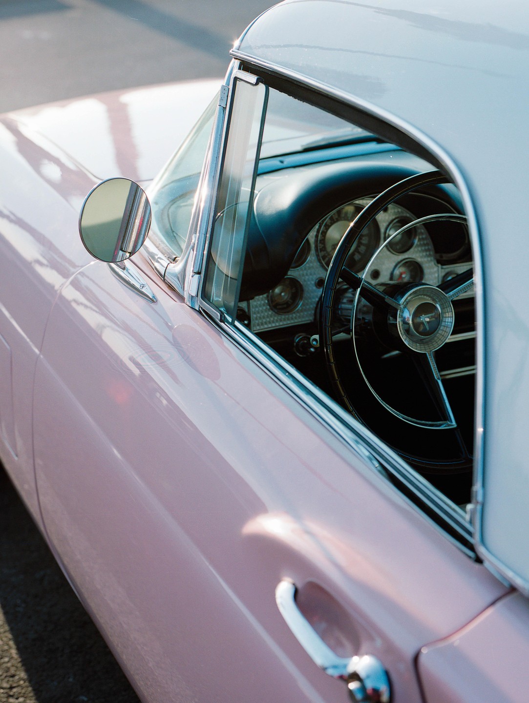 A pink vintage car is parked with its steering wheel and dashboard visible through the window.