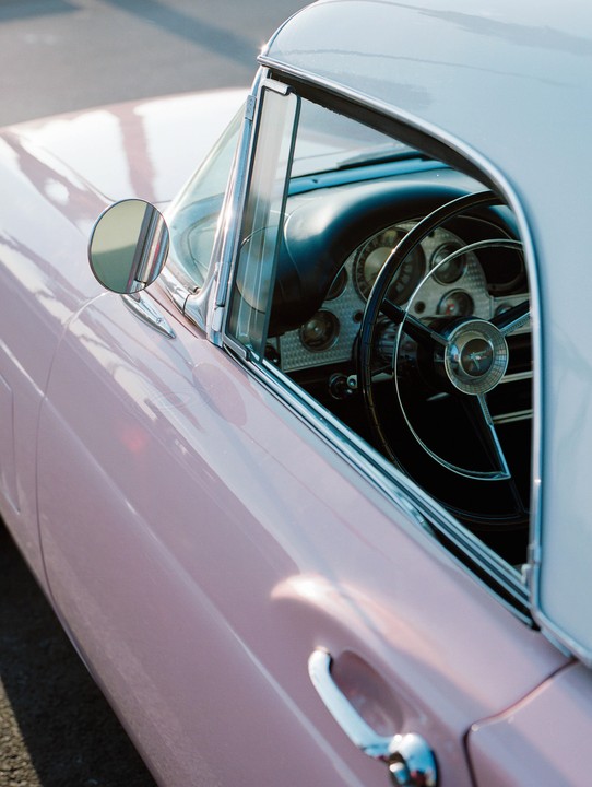 A pink vintage car is parked with its steering wheel and dashboard visible through the window.