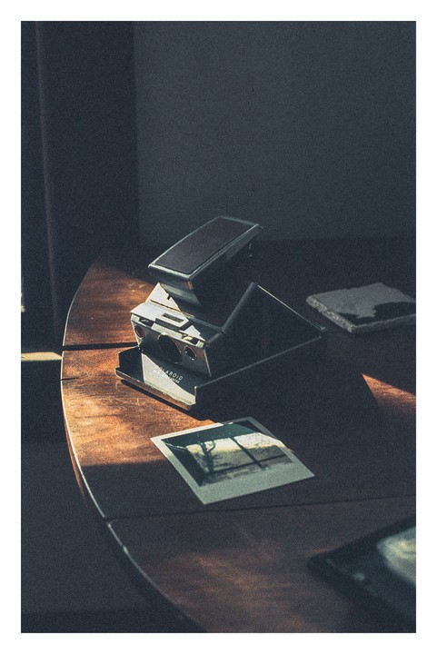 A vintage instant camera and a developed instant photo sit on a wooden table bathed in sunlight.