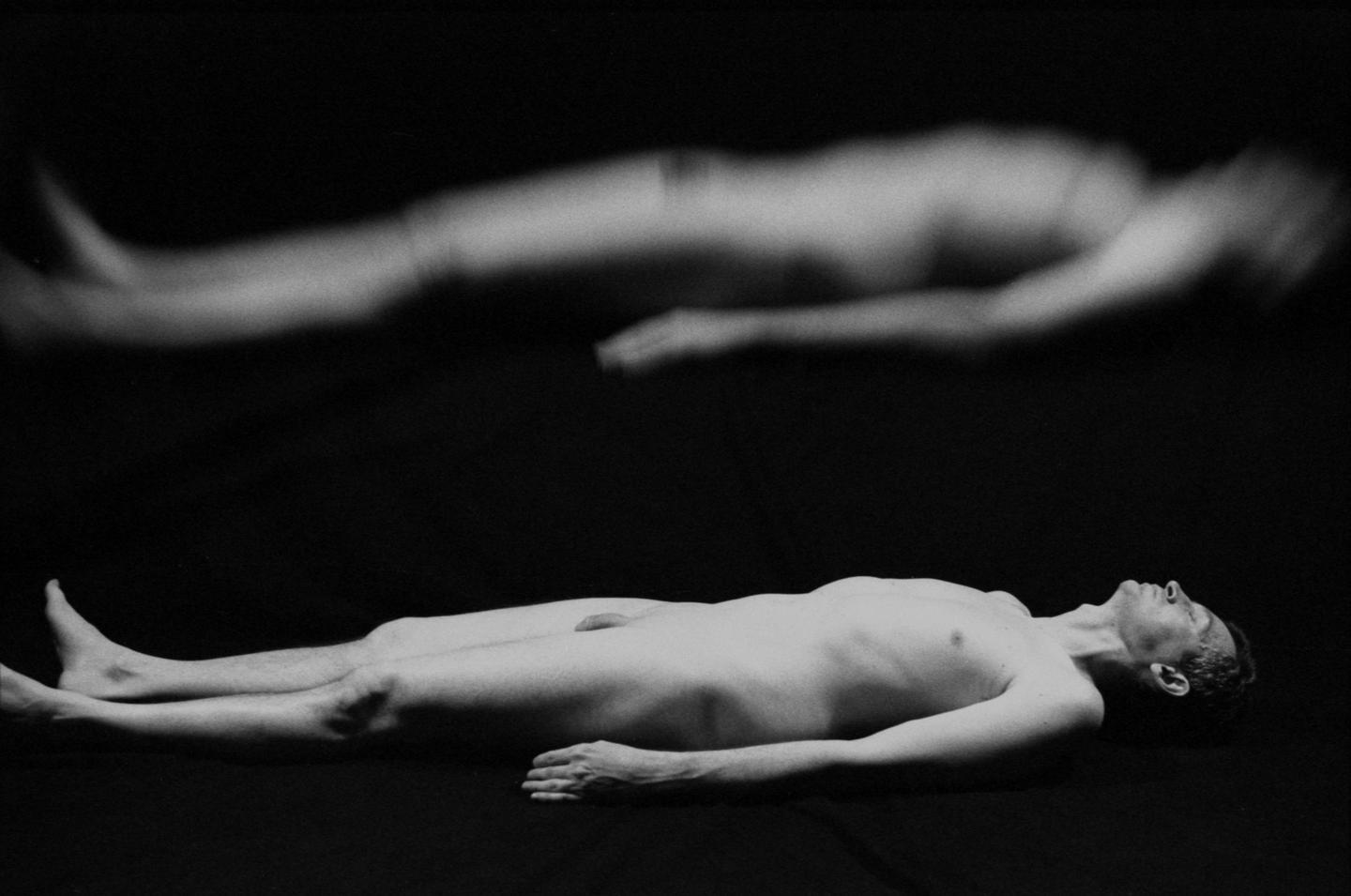 A man lies on his back with his eyes closed, and above him is a blurry, ghost-like double exposure of his body.