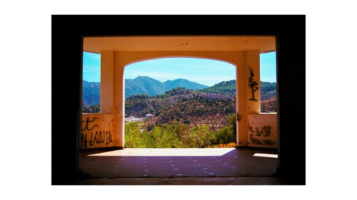 A view of a mountainous landscape with a village from inside a building with graffiti on its walls.