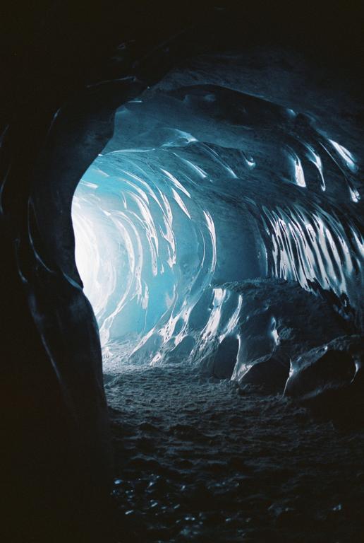 A tunnel of ice with blue light at the end is visible from a dark cave.