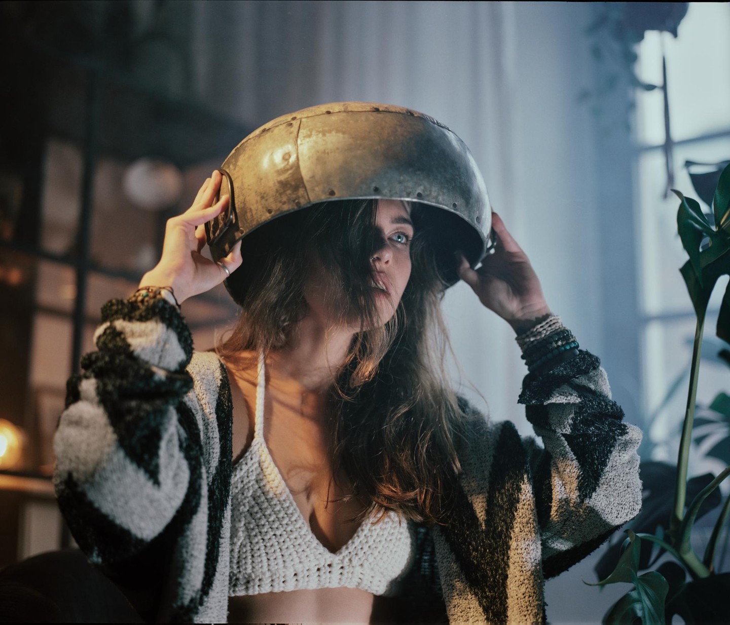 A woman with long hair wears a metal bowl on her head and a crocheted top.