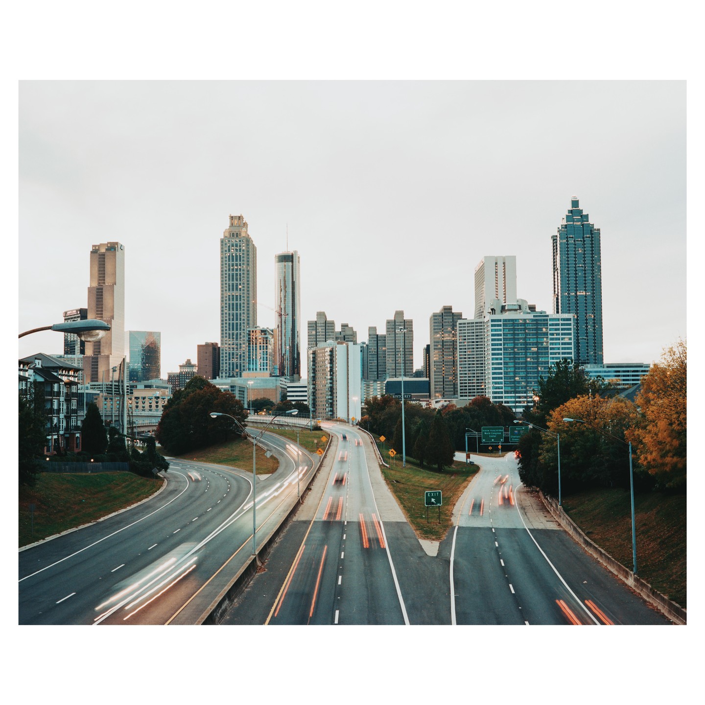 A highway with light trails from cars leads into a city skyline with tall buildings.