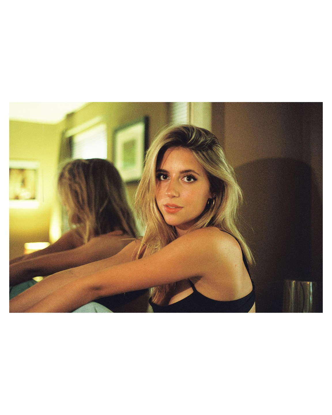A woman with blonde hair sits in front of a mirror, looking at the viewer.