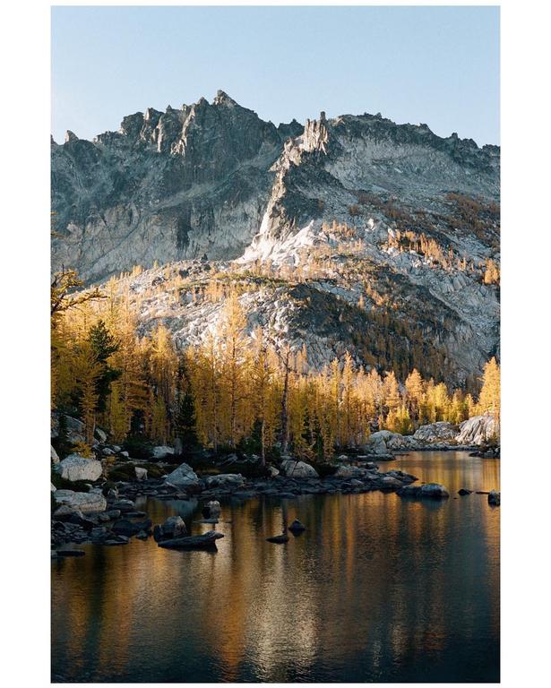 A mountain range with golden trees is reflected in a lake.
