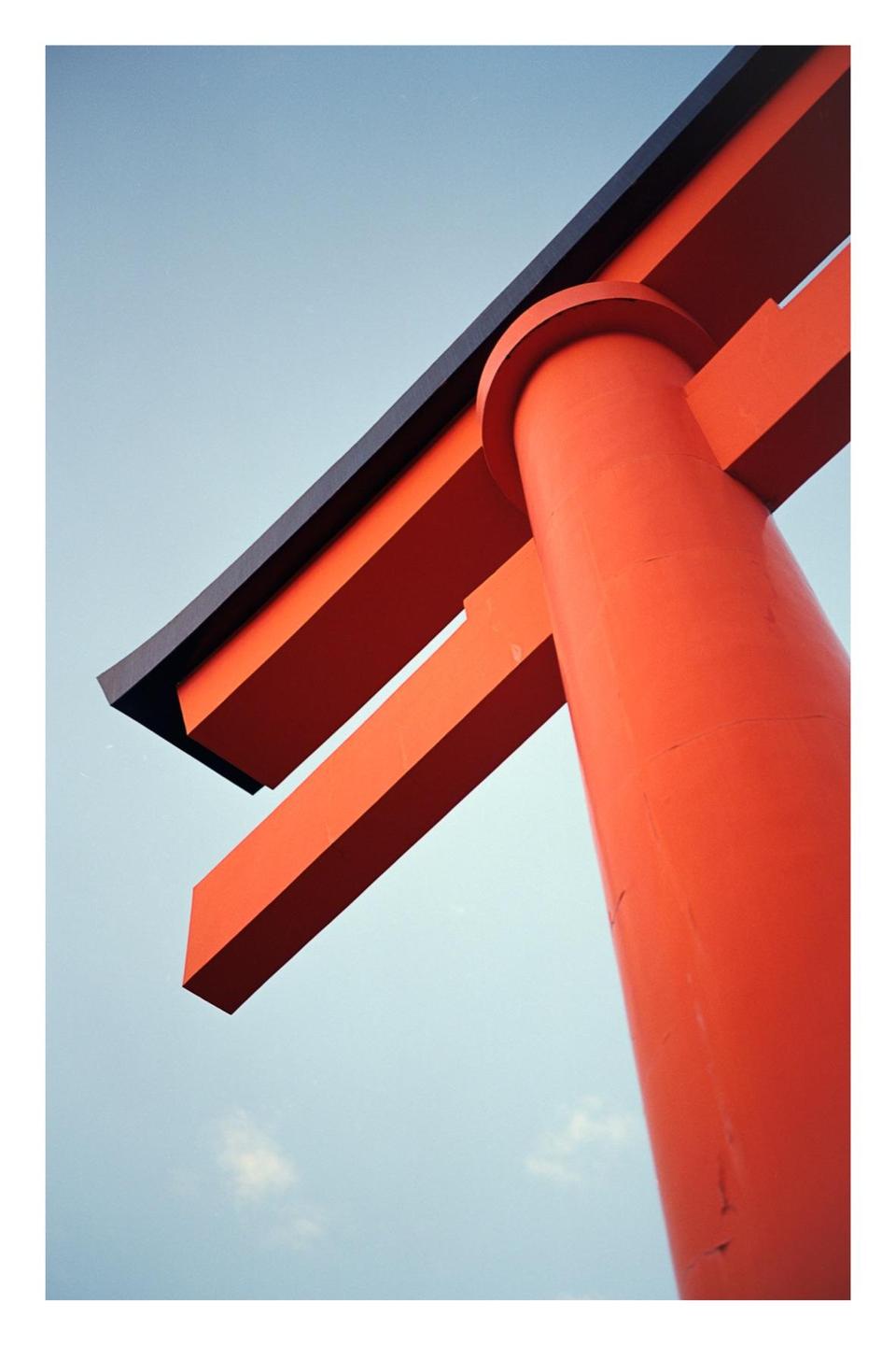 A low-angle view shows a bright orange torii gate against a clear blue sky.
