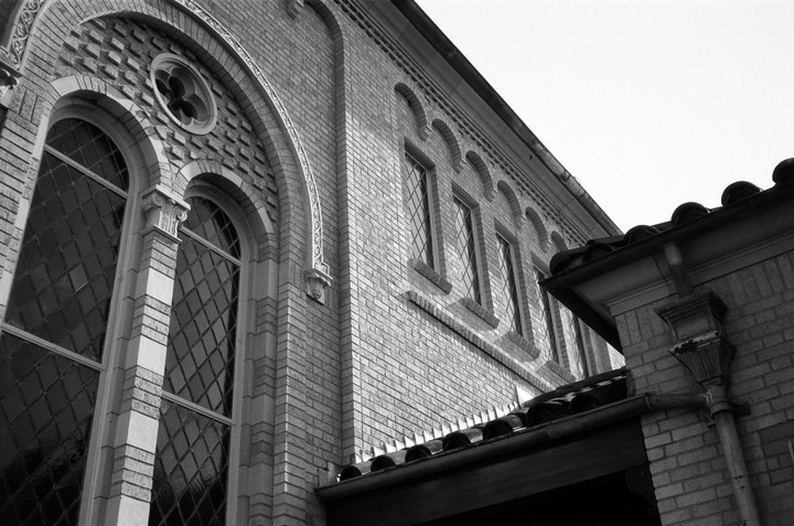 A low-angle view shows the brick facade of a building with arched windows and a tiled roof.