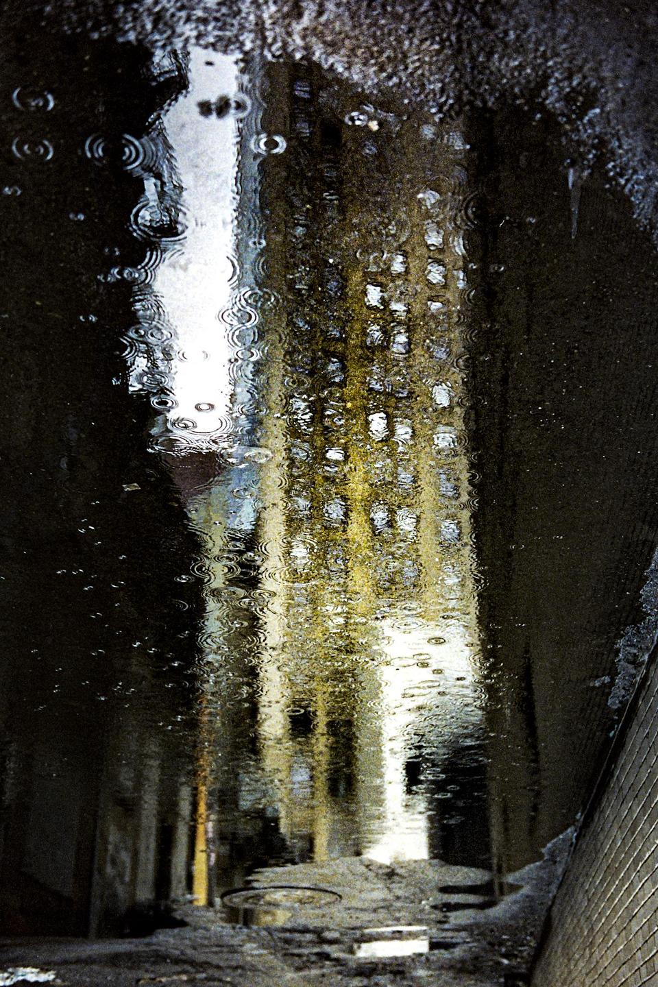 A building is reflected in a puddle with ripples from falling rain.