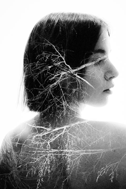 A woman's profile is overlaid with a pattern of tree branches in a double exposure.