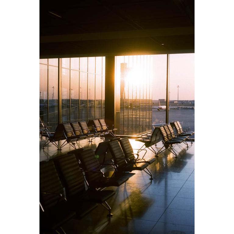 Sunlight streams through large windows into an airport waiting area with rows of empty chairs.