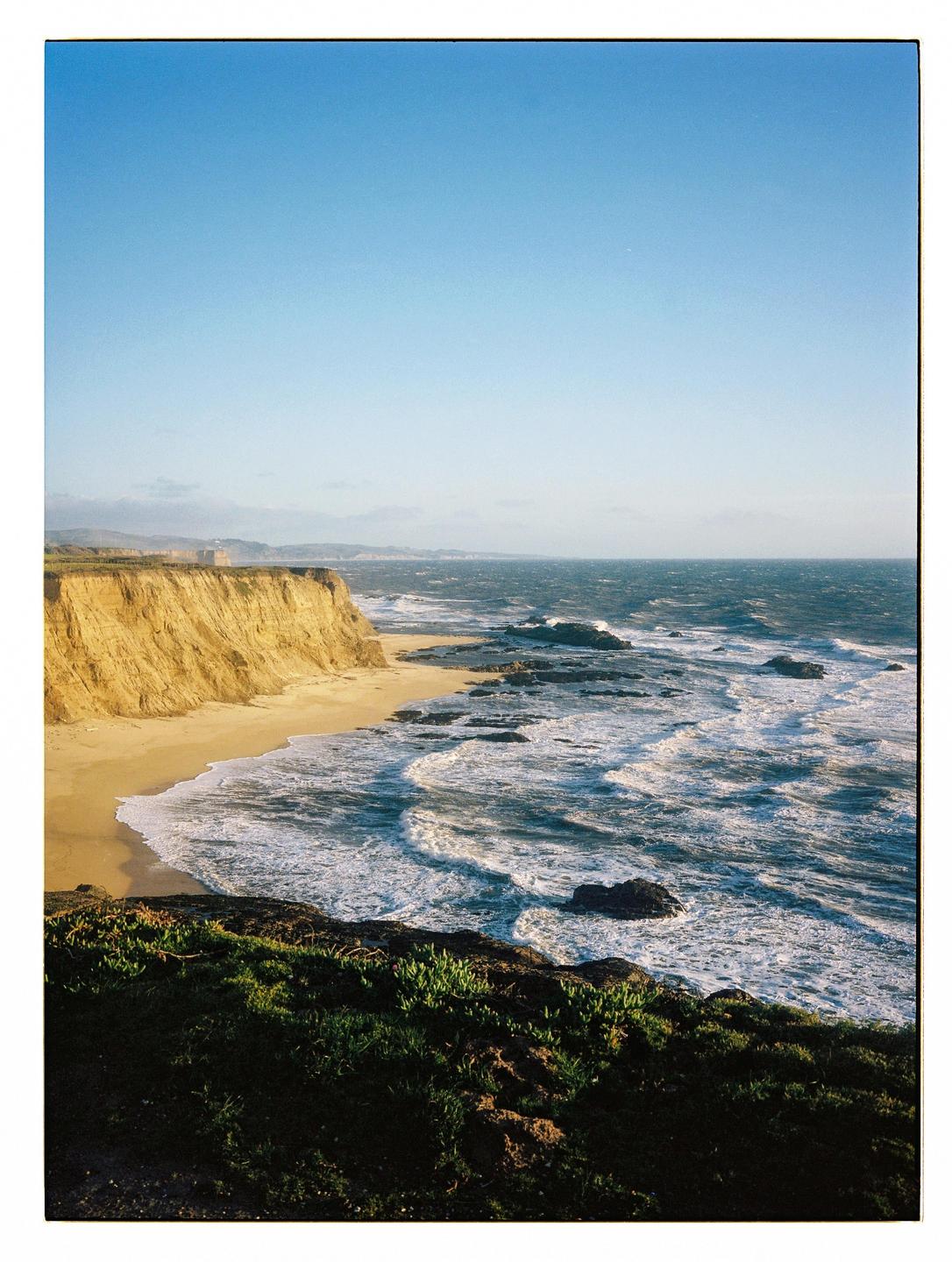 A cliff overlooks a sandy beach with waves crashing on the shore.