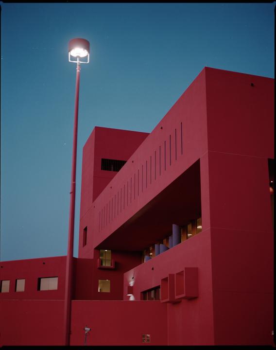 A red building with a tall street light stands against a blue sky.