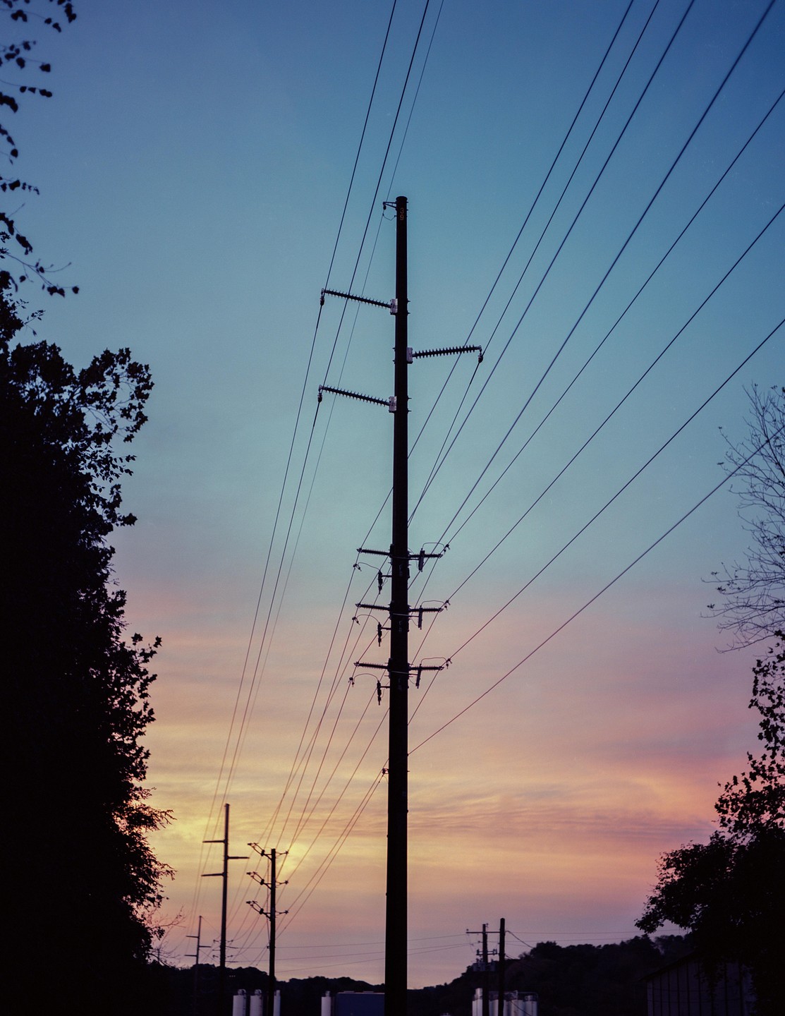 Power lines and utility poles are silhouetted against a colorful sunset sky.