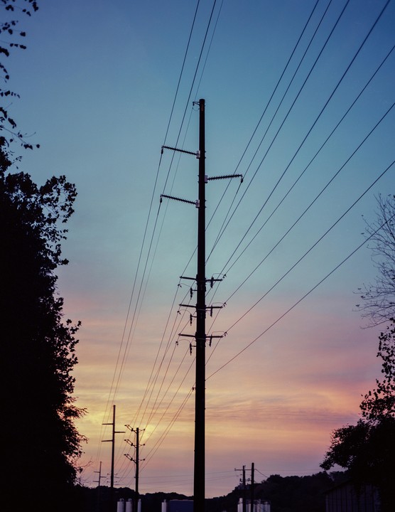 Power lines and utility poles are silhouetted against a colorful sunset sky.