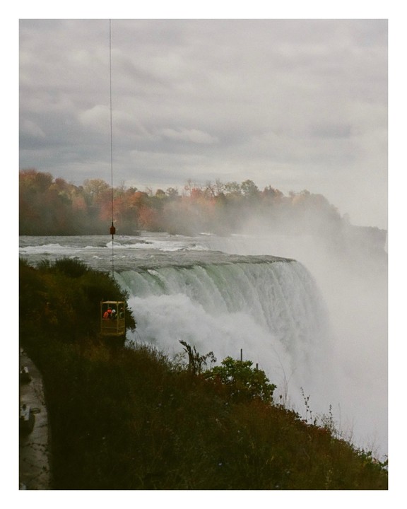 A wide view of Niagara Falls shows the water cascading over the edge, with mist rising and autumn trees in the background.