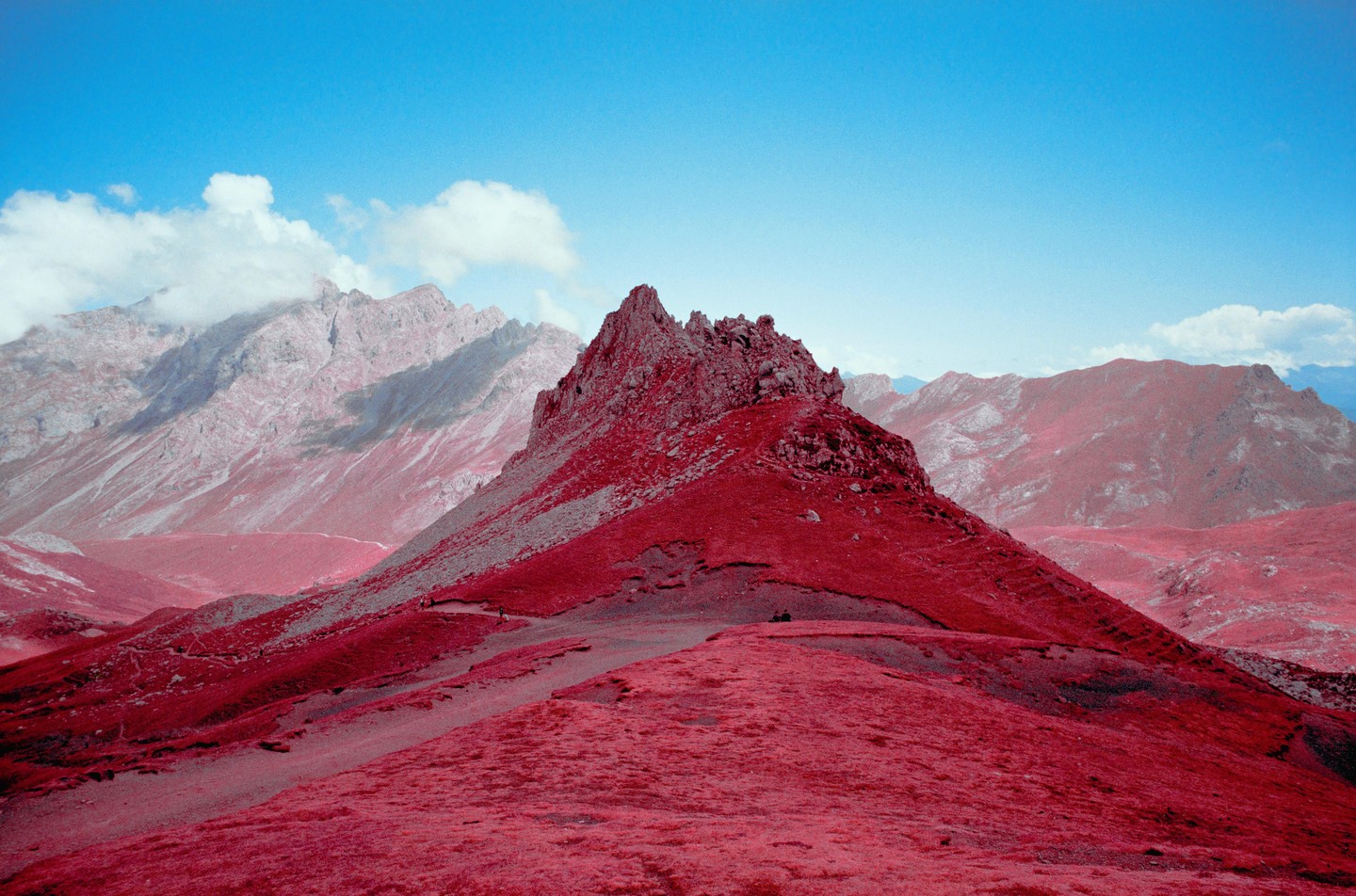 A vibrant red mountain range with a bright blue sky and white clouds.