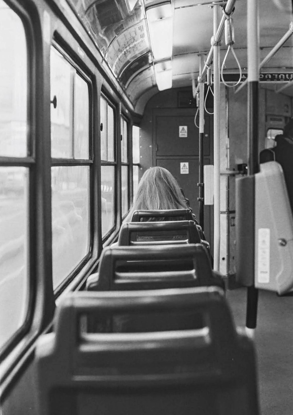 A person with long hair sits in a bus looking out the window.