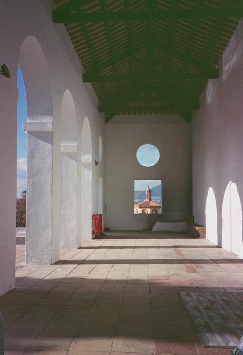 A long, white-walled hallway with a green ceiling leads to a window looking out at a building with a dome.