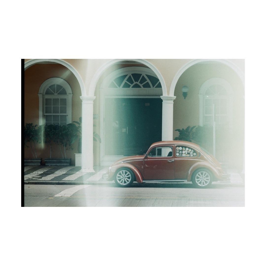 A red beetle car is parked in front of a building with arches and columns.