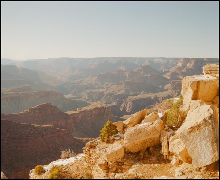 A vast canyon landscape with layered rock formations stretches into the hazy distance under a clear sky.