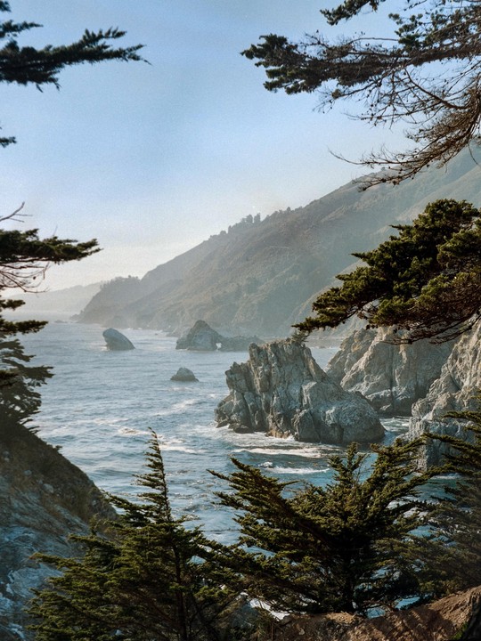 A scenic view of a rugged coastline with mountains, ocean, and rocky outcrops.