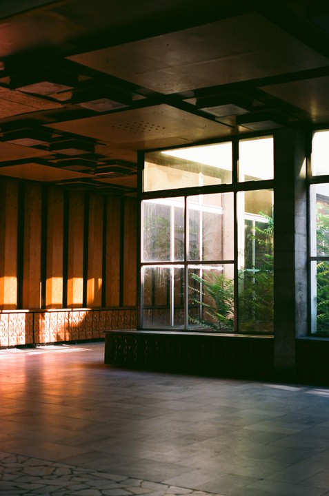 Sunlight streams through a large window into a room with a patterned ceiling and a tiled floor.