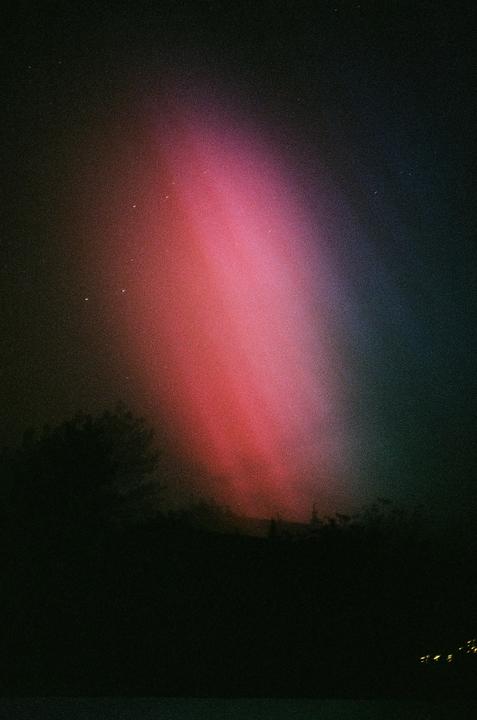 A vibrant red and purple aurora borealis illuminates the night sky above a dark landscape with silhouetted trees.