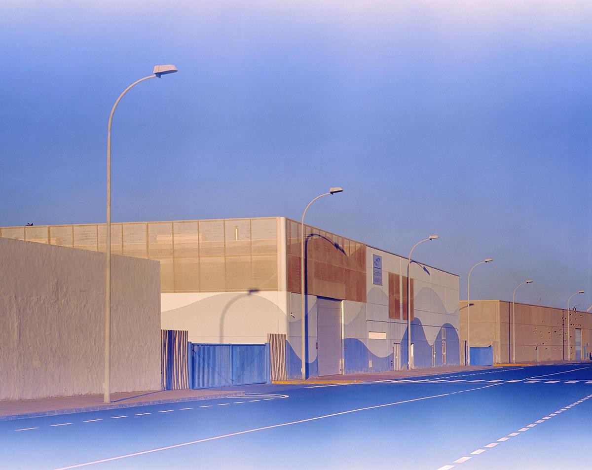 A street with several industrial buildings and streetlights is shown under a clear sky.