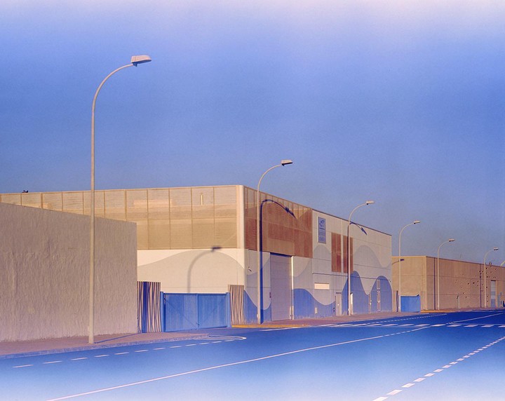 A street with several industrial buildings and streetlights is shown under a clear sky.