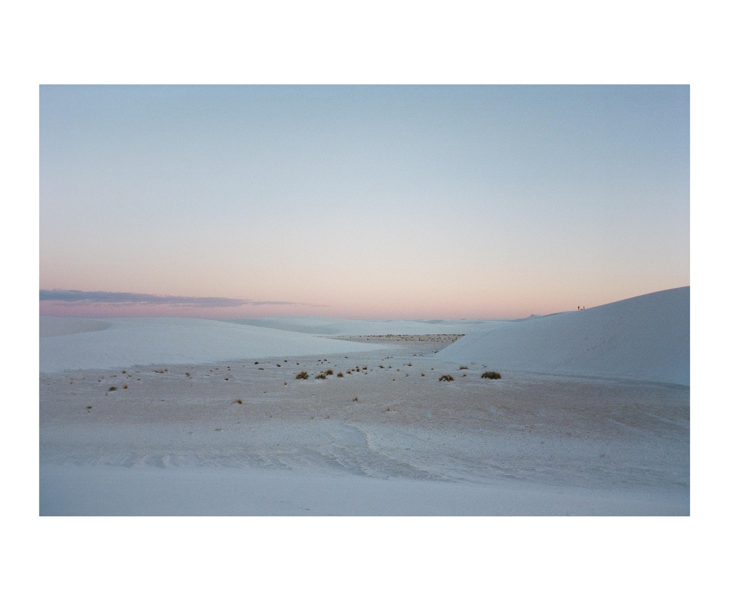 A vast desert landscape with white sand dunes stretches under a sky with hues of pink and blue.